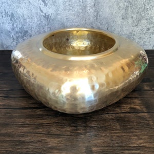 May include: A hammered gold metal planter with a square shape and a rounded, bowl-like top.