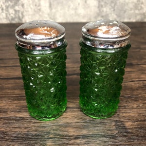 May include: A set of two green glass salt and pepper shakers with silver tops. The shakers have a diamond pattern.