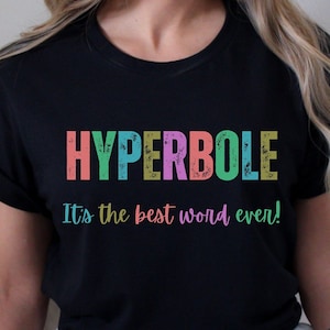 May include: Black t-shirt with the word "HYPERBOLE" in colorful letters. Below the word is the phrase "It's the best word ever!" in a matching colorful font. The shirt is a casual style.