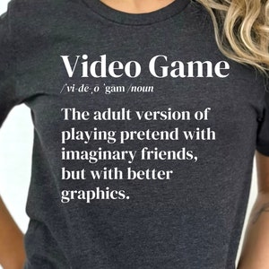 May include: Dark gray t-shirt with the text "Video Game" and a definition. The definition reads: "The adult version of playing pretend with imaginary friends, but with better graphics."