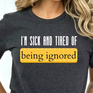 May include: Dark gray t-shirt with the text "I'M SICK AND TIRED OF being ignored" in white and yellow. The shirt is a crew neck style and appears to be made of a soft material.