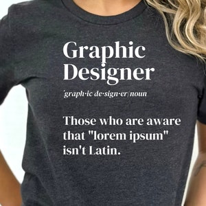 May include: Dark gray t-shirt with the text "Graphic Designer" in white, along with a definition and a statement about "lorem ipsum." The shirt is a crew neck style.