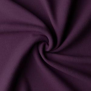 Puede incluir: Primer plano de una tela morada oscura, dispuesta en espiral. El material tiene un aspecto suave y texturizado, con sutiles variaciones tonales. Se destaca el color intenso y la textura suave de la tela.