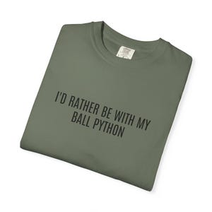 Op de afbeelding: Olijfgroen T-shirt met de zwarte tekst "I'D RATHER BE WITH MY BALL PYTHON". Het shirt is opgevouwen en heeft een label op de kraag.
