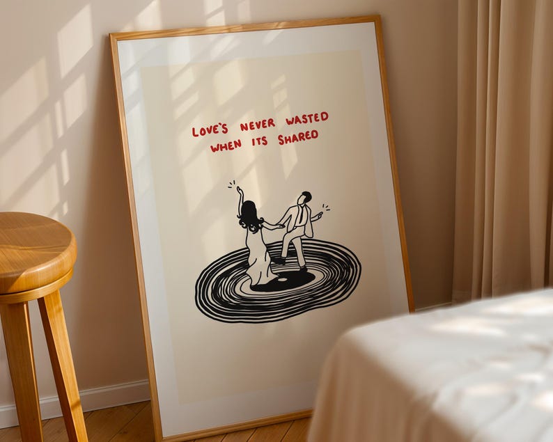 Pode incluir: Uma impress&atilde;o art&iacute;stica emoldurada com fundo creme e um desenho de linhas pretas de duas pessoas a dan&ccedil;ar num disco de vinil. O texto vermelho acima das figuras diz: "LOVE'S NEVER WASTED WHEN ITS SHARED." A moldura &eacute; de madeira clara.