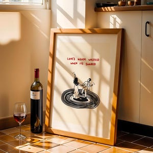 Pode incluir: Uma impress&atilde;o art&iacute;stica emoldurada com uma ilustra&ccedil;&atilde;o a preto e branco de duas figuras a dan&ccedil;ar num disco de vinil. O texto acima das figuras diz "LOVE'S NEVER WASTED WHEN ITS SHARED" em letras vermelhas. Moldura de madeira clara.
