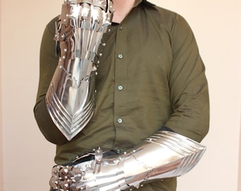 May include: A pair of shiny, silver metal gauntlets. The gauntlets are articulated, with individual plates for the fingers and wrist protection. The metal has a polished finish, reflecting light. The gauntlets are designed to cover the entire hand and forearm.
