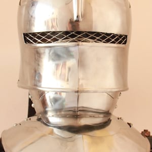 Könnte beinhalten: Ein silberner Helm mit Visier und Nackenschutz. Der Helm hat ein Maschengitter an der Vorderseite.