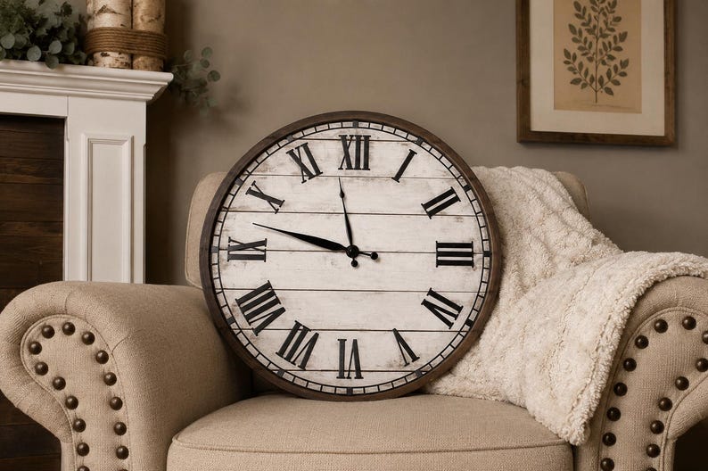 K&ouml;nnte beinhalten: Gro&szlig;e, runde Wanduhr mit einem wei&szlig;en Zifferblatt im Used-Look und schwarzen r&ouml;mischen Ziffern. Die Uhr hat einen dunkelbraunen Holzrahmen und schwarze Zeiger. Die Uhr liegt auf einem beigen Sessel mit einer wei&szlig;en Decke.