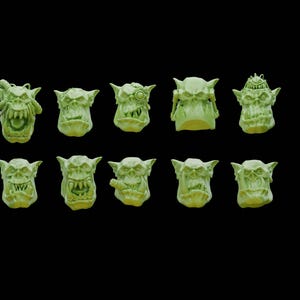 May include: A set of 10 green plastic Orc heads with different expressions. The heads are detailed with teeth, eyes, and other facial features.