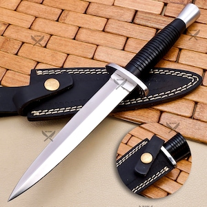 May include: A black and silver dagger with a black leather sheath. The dagger has a textured black handle and a sharp, pointed blade.