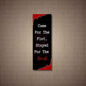 Może przedstawiać: Czarna zakładka do książki z białym napisem "Came For The plot, Stayed For The smut". Zakładka ma czerwony wzór na górze i na dole.