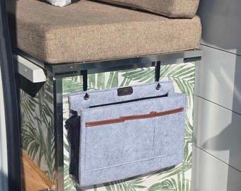 May include: A gray felt hanging organizer with multiple pockets and a brown leather trim. The organizer is hanging on a metal bar in a van with a tropical leaf patterned wall.