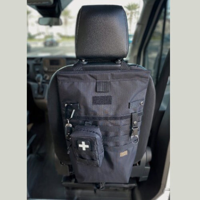 May include: Black tactical seatback organizer with multiple pockets and compartments. It includes a small first aid kit with a white cross.