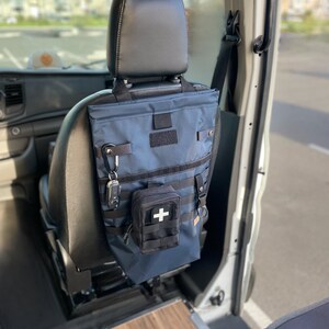 May include: A blue and black travel bag with a first aid kit hanging from the front. The bag is hanging on the back of a car seat.