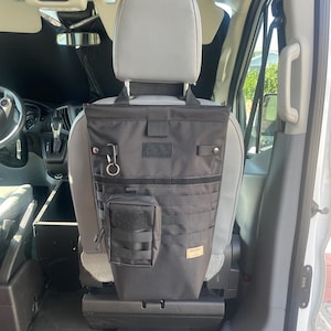 Puede incluir: Organizador de asiento negro con múltiples bolsillos y puntos de fijación, colgado del reposacabezas de un asiento de vehículo. Incluye una pequeña bolsa y un mosquetón. El organizador está diseñado para el almacenamiento.