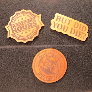 May include: Three wooden stickers with humorous text. One reads "Working All Day Overtime Hours For Bullshit Pay", another says "But Did You Die?", and the last one says "Danger Zone Liberty or Death".