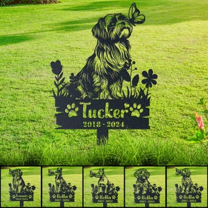 May include: Black metal silhouette of a dog with a butterfly, flowers, and a sign that reads "Tucker 2018-2024". This is a garden memorial for a pet.