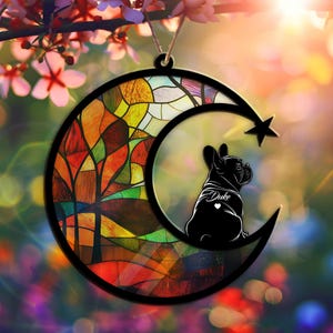 May include: A stained glass moon ornament with a silhouette of a French Bulldog. The moon has a colorful stained glass design with a star at the top. The dog is black and has the name "Duke" written on its back.