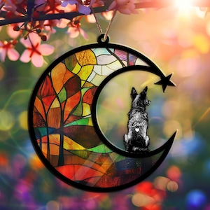 May include: A crescent moon-shaped ornament with a stained-glass design and a black dog silhouette. The ornament features a star and the dog's name, "Duke," with a heart. The stained glass has red, orange, yellow, and green colors.