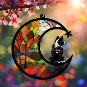 May include: A stained glass moon ornament with a black and white dog silhouette inside. The moon has a colorful stained glass design with red, orange, yellow, green, and blue colors. The dog is sitting on the moon and has the name "Duke" written on its chest.