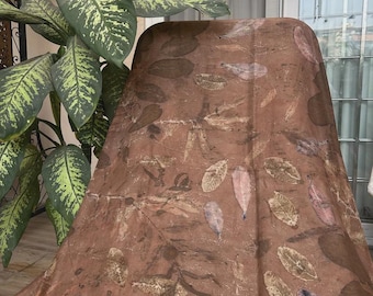 May include: A rectangular fabric scarf featuring a warm brown base color with a repeating pattern of various leaf imprints in shades of tan, dark brown, and muted purple. The textile displays a natural, organic aesthetic with visible leaf veins.
