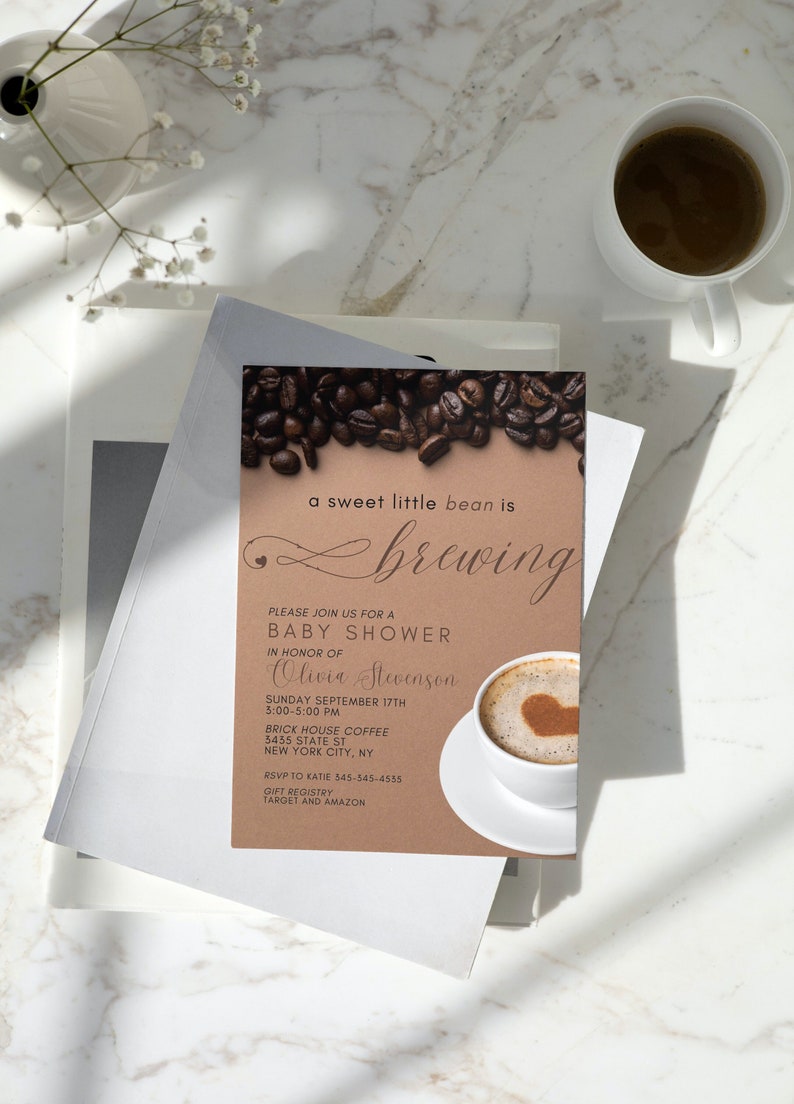 May include: A brown invitation card with a coffee bean border and a cup of coffee with a heart design in the foam. The text reads "a sweet little bean is brewing" and includes details for a baby shower for Olivia Stevenson.