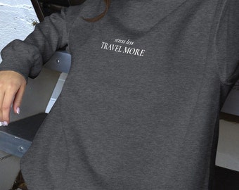 Könnte beinhalten: Ein dunkelgrauer Pullover mit dem Text "stress less TRAVEL MORE" in Weiß.