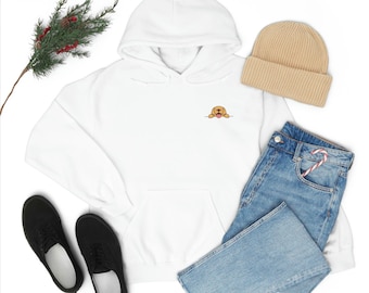Op de afbeelding: Witte hoodie met een klein geborduurd beeld van een golden retriever puppy die over de rand kijkt met zijn tong naar buiten. De hoodie ligt op een witte achtergrond met een paar zwarte sneakers, een blauwe jeans en een beige beanie.