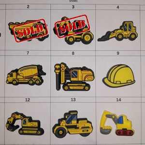 May include: A collection of yellow and black construction vehicle charms, including excavators, a cement mixer, and a crane. Some charms have a red "SOLD" stamp. A yellow hard hat is also featured.