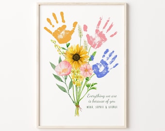 May include: A framed print with a watercolor illustration of a bouquet of flowers with handprints in yellow, pink, and blue. The text reads "Everything we are is because of you. Noah, Sophie & George."
