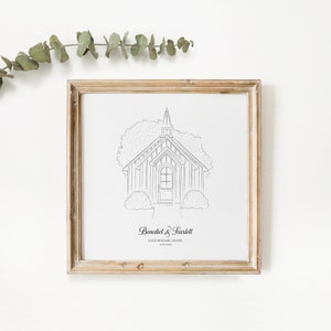 May include: A framed black and white line drawing of a chapel with a steeple, surrounded by trees and bushes. The frame is a light brown color. The text at the bottom reads "Benedict & Scarlett" and "Rockingham Chapel 10.07.2023".