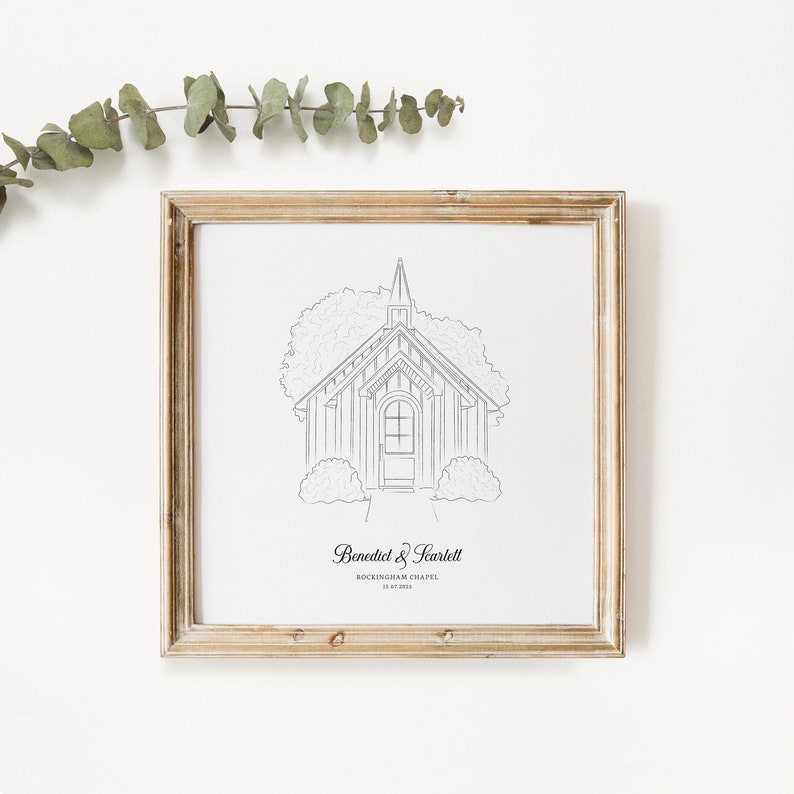 May include: A framed black and white line drawing of a chapel with a steeple, surrounded by trees and bushes. The frame is a light brown color. The text at the bottom reads "Benedict & Scarlett" and "Rockingham Chapel 10.07.2023".