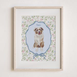 May include: Framed print featuring a dog illustration. The dog, with brown and white fur, is centered within a light blue, ornate frame. The background is a floral pattern with pink and blue flowers. The dog's name, "Kipper", is written above.