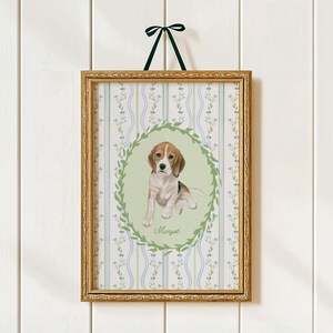 May include: A framed print featuring a beagle puppy illustration. The artwork is set within a gold-colored frame and is suspended by a dark green ribbon. The background has a floral pattern with blue and green accents. The puppy is surrounded by a green wreath and the name "Margot" is written below.
