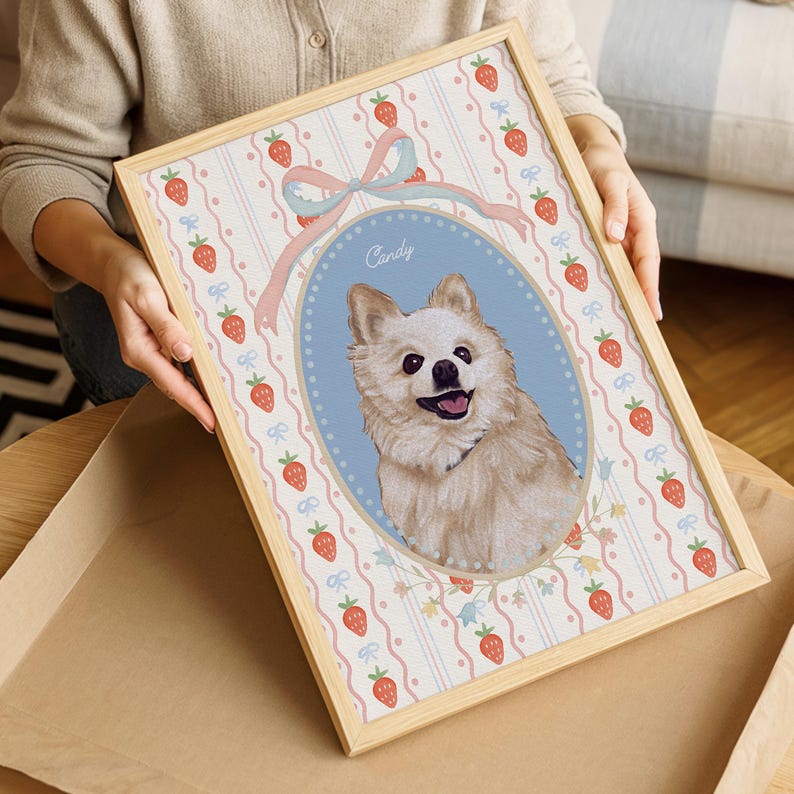 May include: A framed portrait of a fluffy, light-colored dog named Candy. The artwork is set against a light blue background with a pink and white striped pattern, adorned with strawberries and bows. The frame is made of light-colored wood.