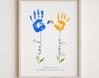 May include: A white framed print with two handprints, one blue and one yellow, with the names "Noah" and "George" written underneath. The text "Hands up for the world's greatest dad!" is at the bottom of the print.