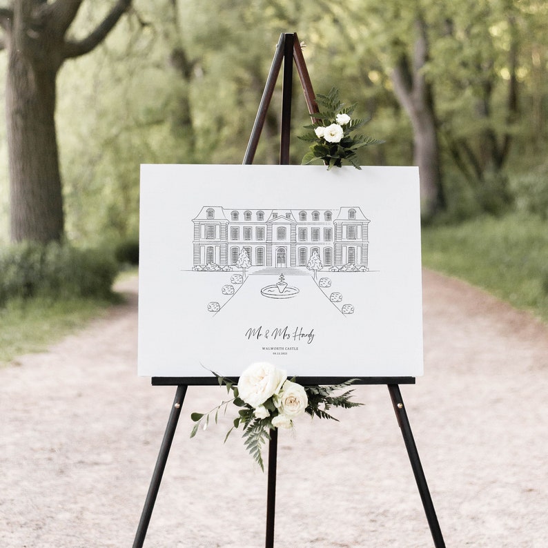 May include: A white sign on a black easel displays a detailed line drawing of a stately building with a fountain and landscaping. The sign reads "Mr. & Mrs. Hardy" and "Walworth Castle". White flowers and greenery adorn the easel.