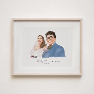 May include: A framed portrait of two people, one in a blue suit and glasses, the other in a white wedding dress. The words "Happy Anniversary" are written in cursive below the portraits, with the date 05.09.24. The frame is light wood.