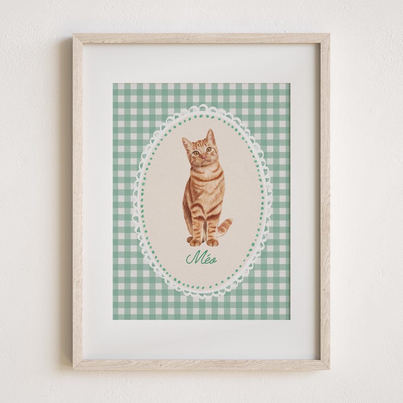 May include: Framed print featuring a watercolor illustration of a tabby cat. The cat is inside an oval frame with a scalloped edge, set against a green and white gingham background. The word "M&eacute;a" is written in script below the cat.