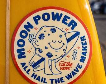 Puede incluir: Una pegatina circular sobre una superficie amarilla con un personaje de luna de dibujos animados sosteniendo una tabla de surf. El texto dice MOON POWER, ALL HAIL THE WAVE MAKER, SINCE FOREVER y Eat the wave. Un pequeño alien junto a la luna.
