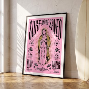 May include: A framed poster with a pink background featuring a central figure with hands together, holding a surfboard labelled FAITH FLOAT. Text includes SURF AND BE SAVED, FIND LOVE, SWIM DEEP, HOLY WATER, and Eat the Wave, with skull and flower icons.