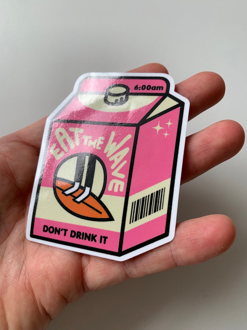 May include: Pink milk carton sticker featuring the text 'Eat the Wave' and 'Don't Drink It'.  The design includes a cartoon surfer and a barcode. The time '6:00am' is printed on the top of the carton. The sticker has a glossy finish.