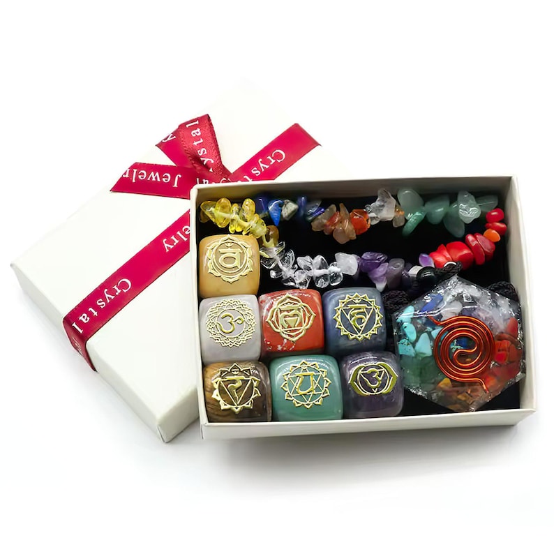 K&ouml;nnte beinhalten: Eine wei&szlig;e Schachtel mit einem roten Band und dem Aufdruck "Crystal Jewelry". Die Schachtel ist ge&ouml;ffnet und enth&auml;lt sieben kleine, farbige, quadratische Steine mit goldenen Symbolen darauf. Au&szlig;erdem befindet sich ein gr&ouml;&szlig;erer, durchsichtiger, mehrfarbiger Stein mit einer Kupferspirale darin.