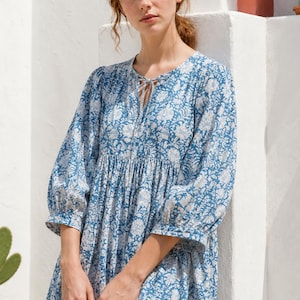May include: A blue and white floral print dress featuring three-quarter length sleeves with gathered cuffs, a round neckline with a small tie closure, and a loose, flowing silhouette that falls above the knee with a gathered waistline detail.