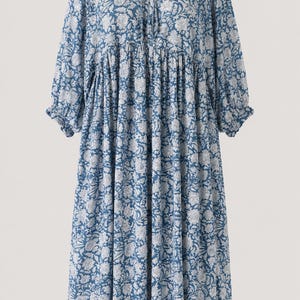 May include: A midi-length dress in a blue and white floral print. The garment features long sleeves with gathered cuffs, a round neckline with a tie closure, and a loose, flowing silhouette with a gathered waistline detail.