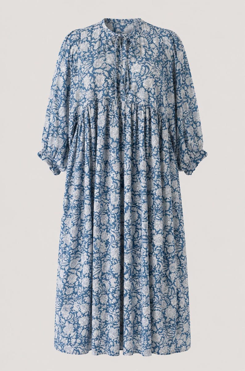 May include: A midi-length dress in a blue and white floral print. The garment features long sleeves with gathered cuffs, a round neckline with a tie closure, and a loose, flowing silhouette with a gathered waistline detail.