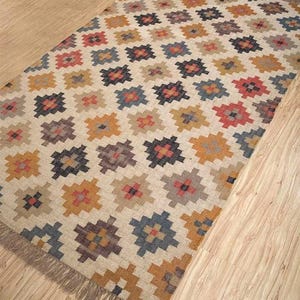 May include: A rectangular rug with a geometric pattern in shades of brown, beige, orange, red, and blue. The rug has a fringe border.