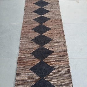 May include: A long, rectangular jute rug with a black and brown diamond pattern. The rug has a fringed edge.
