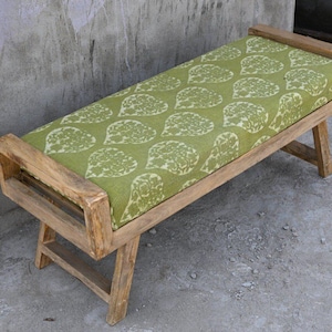 May include: A wooden bench with a rectangular seat cushion. The cushion is green with a white leaf pattern. The bench has a natural wood finish and is supported by angled legs. The bench is approximately 48 inches long.